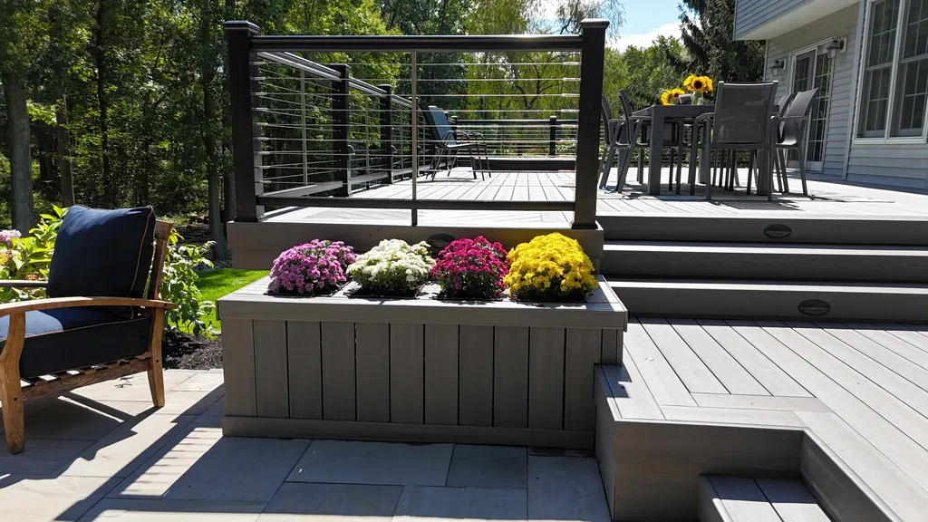 Composite planter box with mums set into deck steps below a cable-rail dining deck