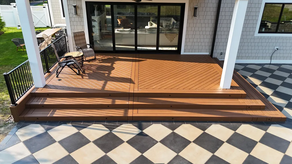 Covered deck with black railing and steps down to a checkerboard paver patio