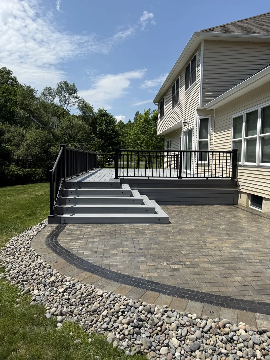 Deck with black railing and stairs down to a curved paver patio, side angle, summer, Orange County, NY