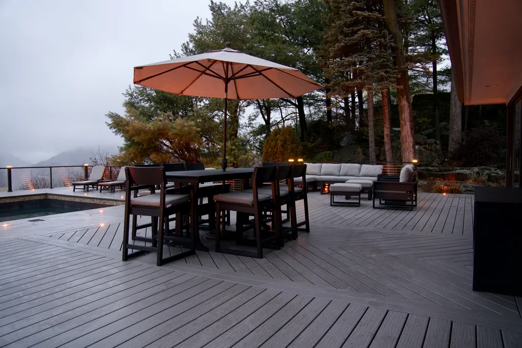 Outdoor dining under an umbrella on a deck beside a pool, with mountains beyond at dusk