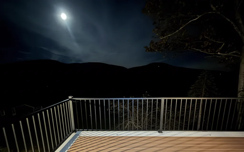 Full moon over the mountains above a deck corner with black railing and white trim boards