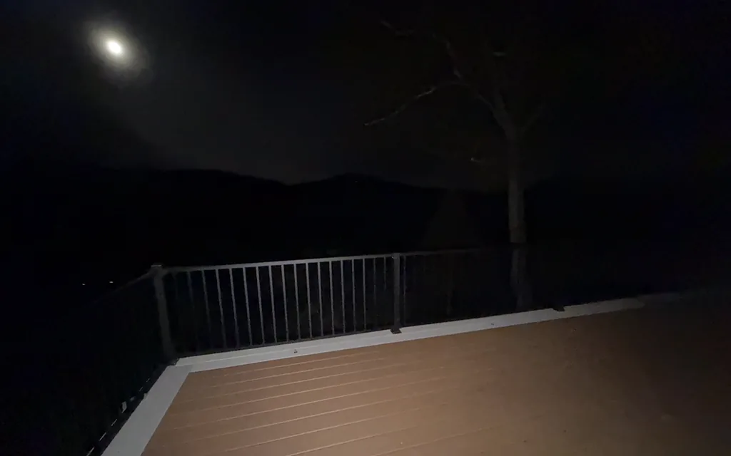Full moon above dark mountains and a deck with black railing at night