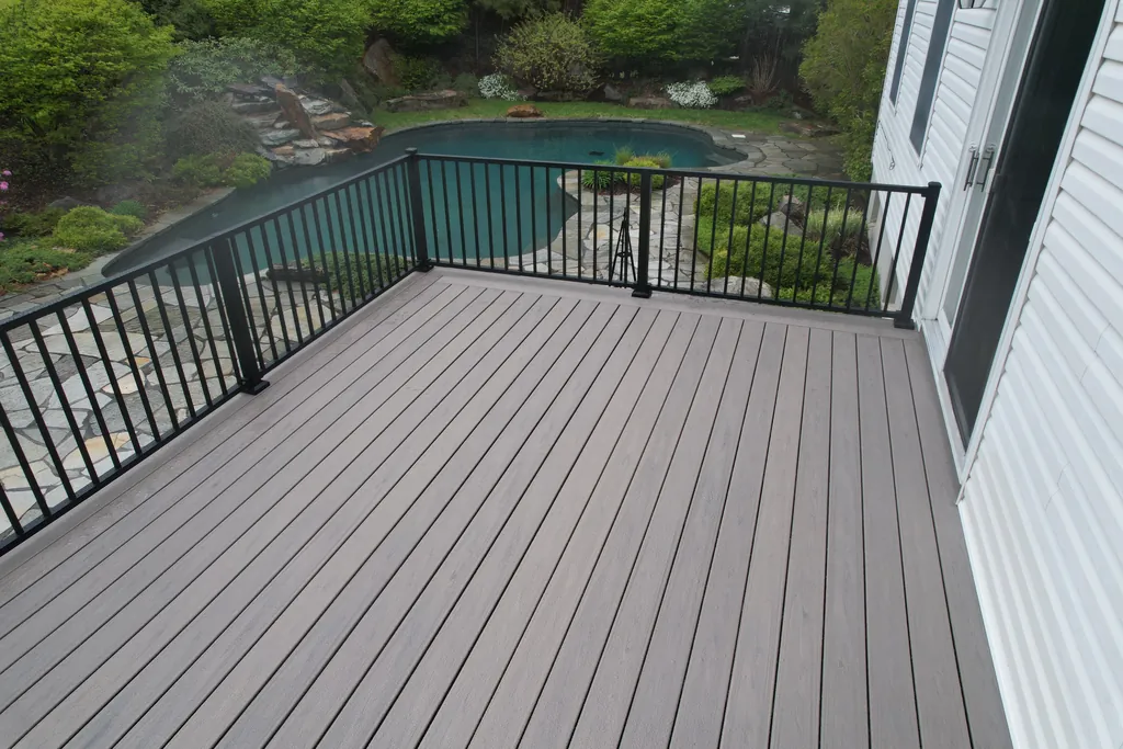 Gray composite deck with black aluminum railing overlooking a pool and garden