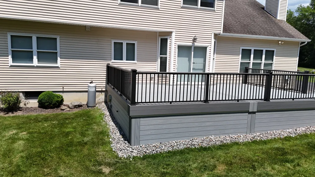 Gray composite deck with black aluminum railing over a gray skirt and stone border