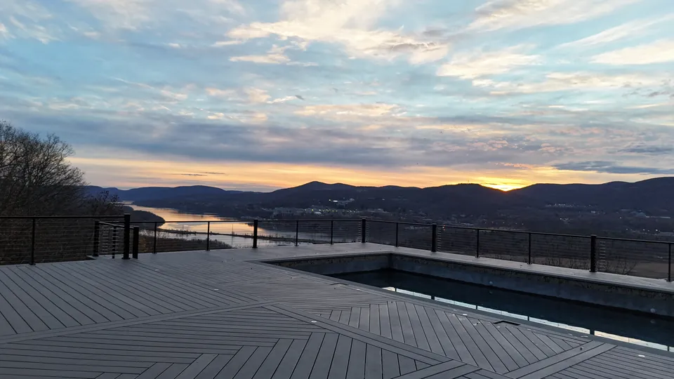 Sunset over the Hudson River and mountains from a pool deck with herringbone decking and black cable railing