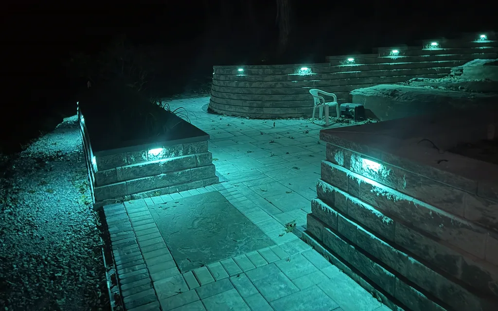 Stone retaining walls with built-in lights glowing over a paver patio at night