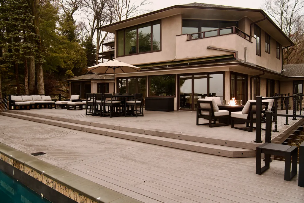 Modern home with a full-width deck, lounge seating and a pool at dusk