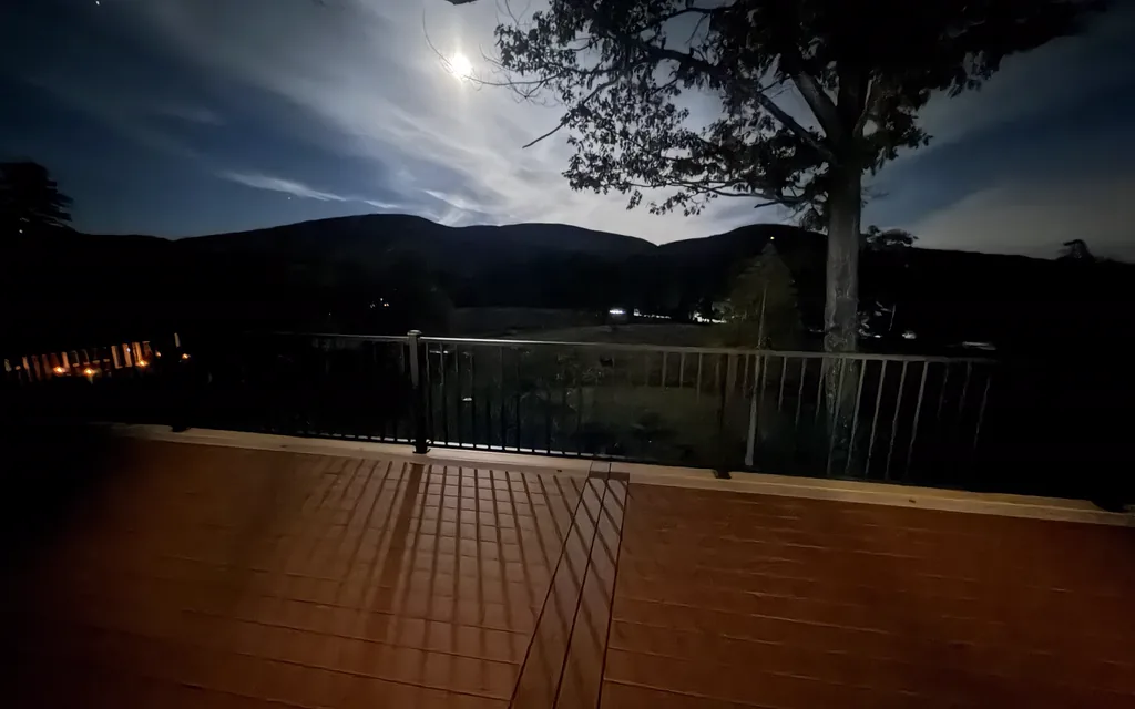 Moonlit deck with black aluminum railing, rail shadows across the boards and mountains on the horizon
