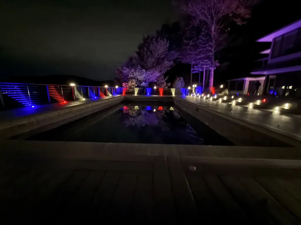 Pool deck at night with red, white and blue railing lights reflected in the water