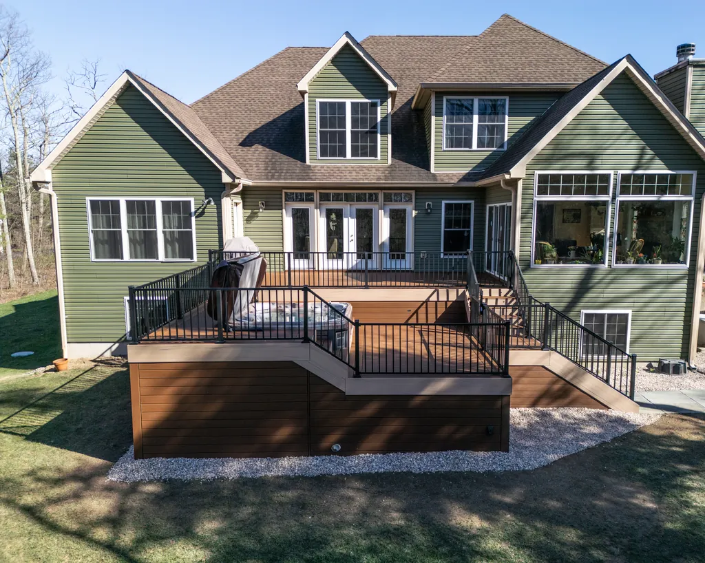 Two-level composite deck with black aluminum railing across the back of a green house