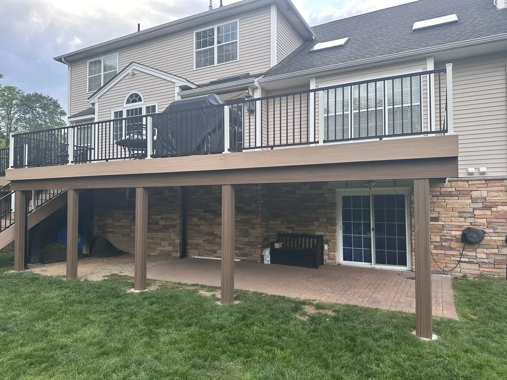 Under-deck view with black structural post-and-beam framing over a stacked-stone foundation and paver patio, Dutchess County, NY